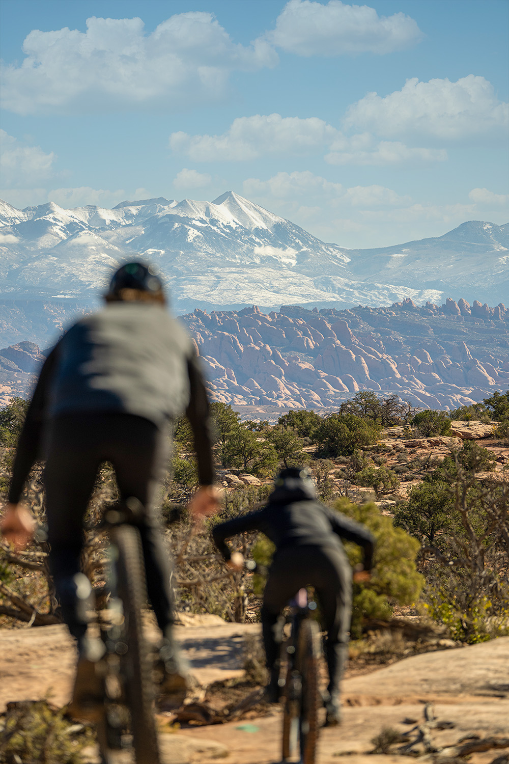 Eric and Libby riding away from the camera. They are out of focus and the background is in focus, which is snow covered mounntains.