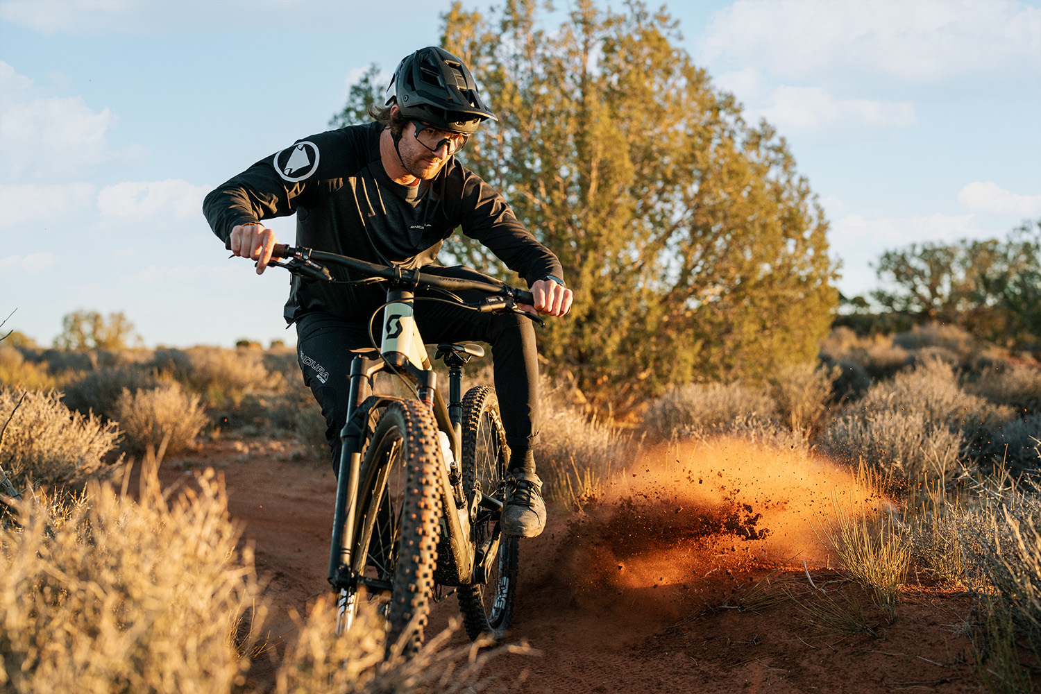 Eric riding towards the camera looking to the side of the camera with a dirt roost.