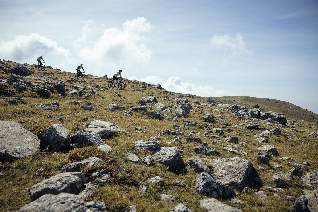 Three mountain bikers riding on stones and going down