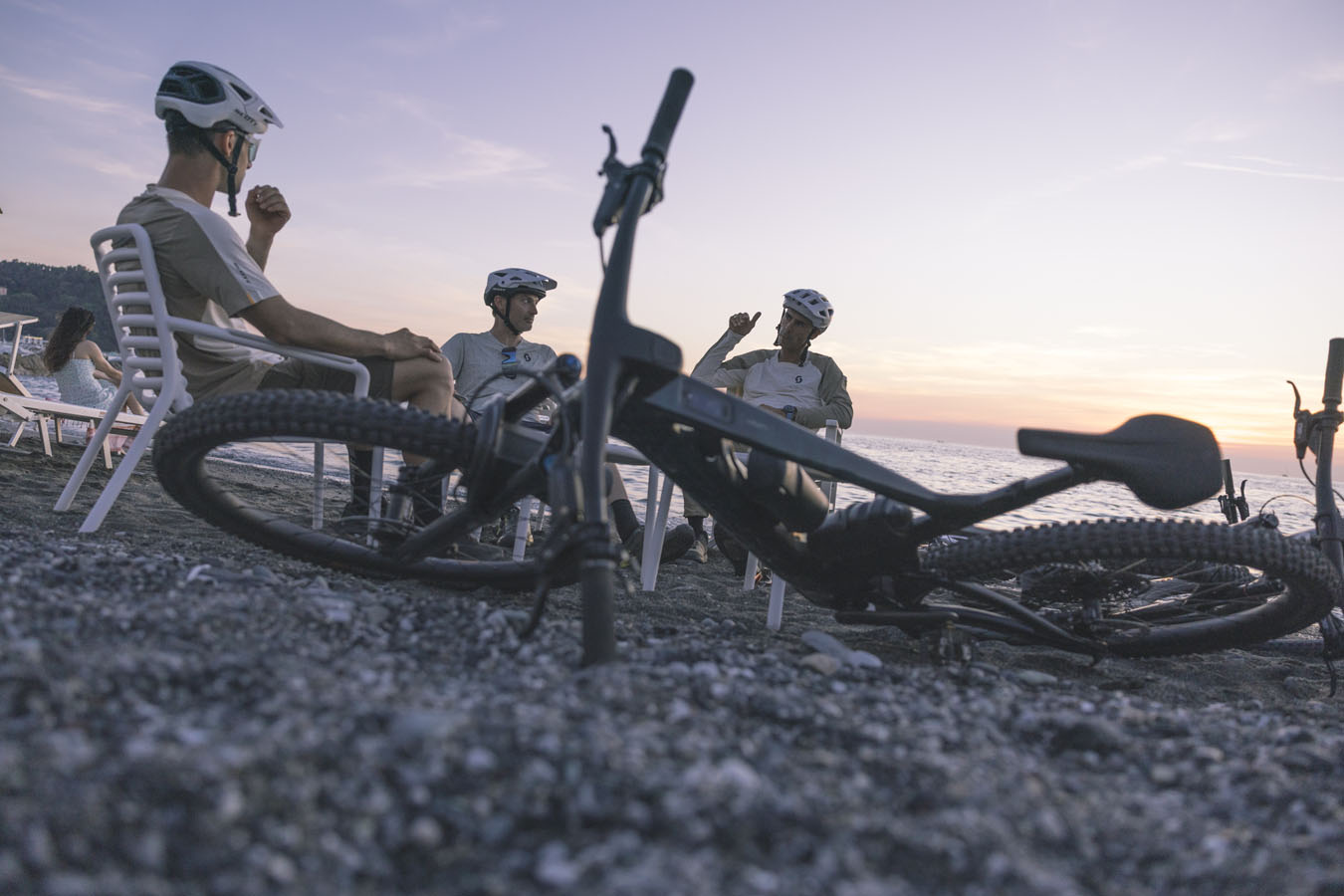Three mountain bikers sitting on a beach and discussing