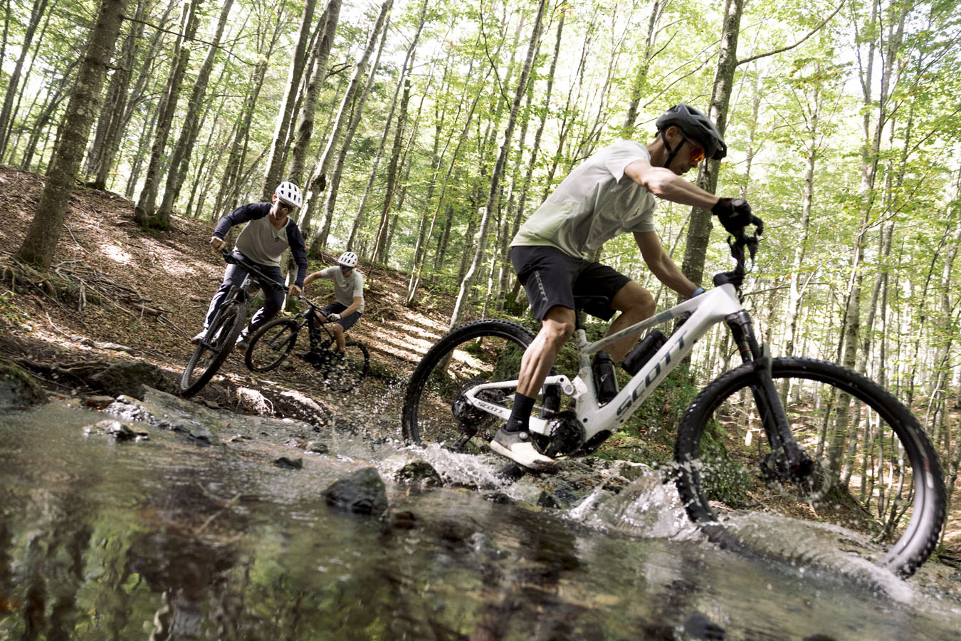 Three mountain bikers riding in the forest on is riding in the water