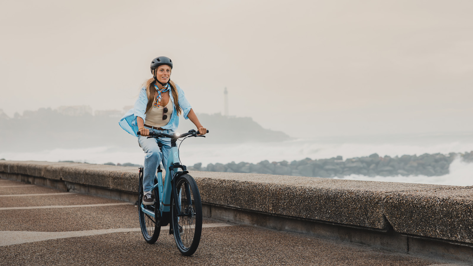 Woman smiling while rding a SCOTT e-bike at the beach.