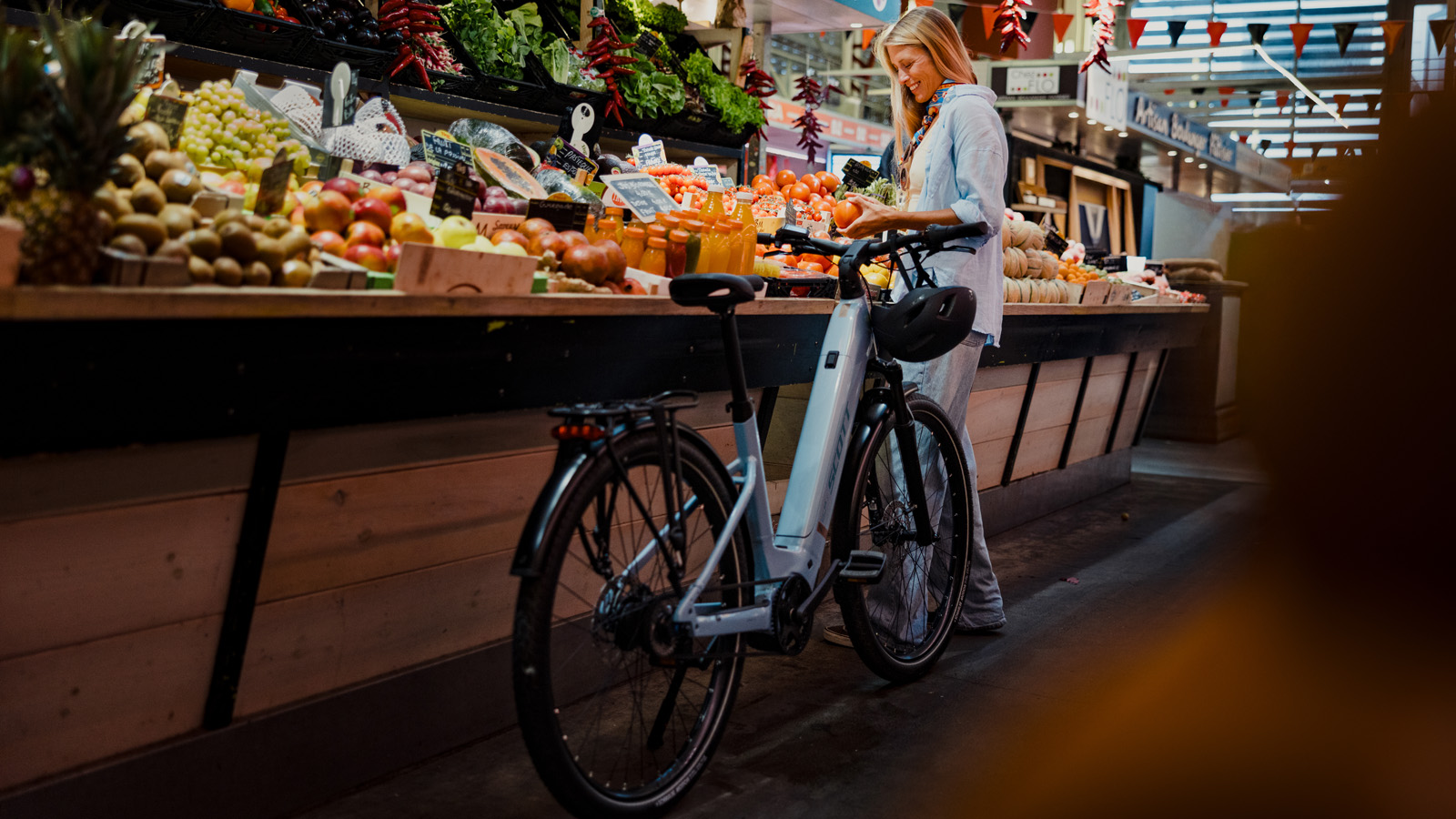 Woman at the market picking up fruits while smiling and standing next to her SCOTT e-bike