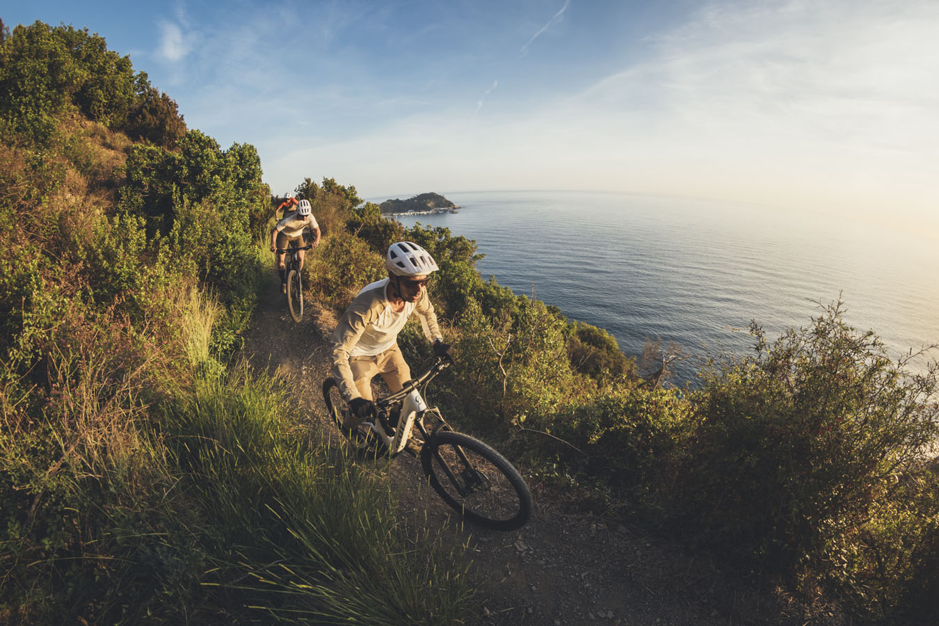 Three mountain bikers riding in front of the sea on a singletrack very narrow
