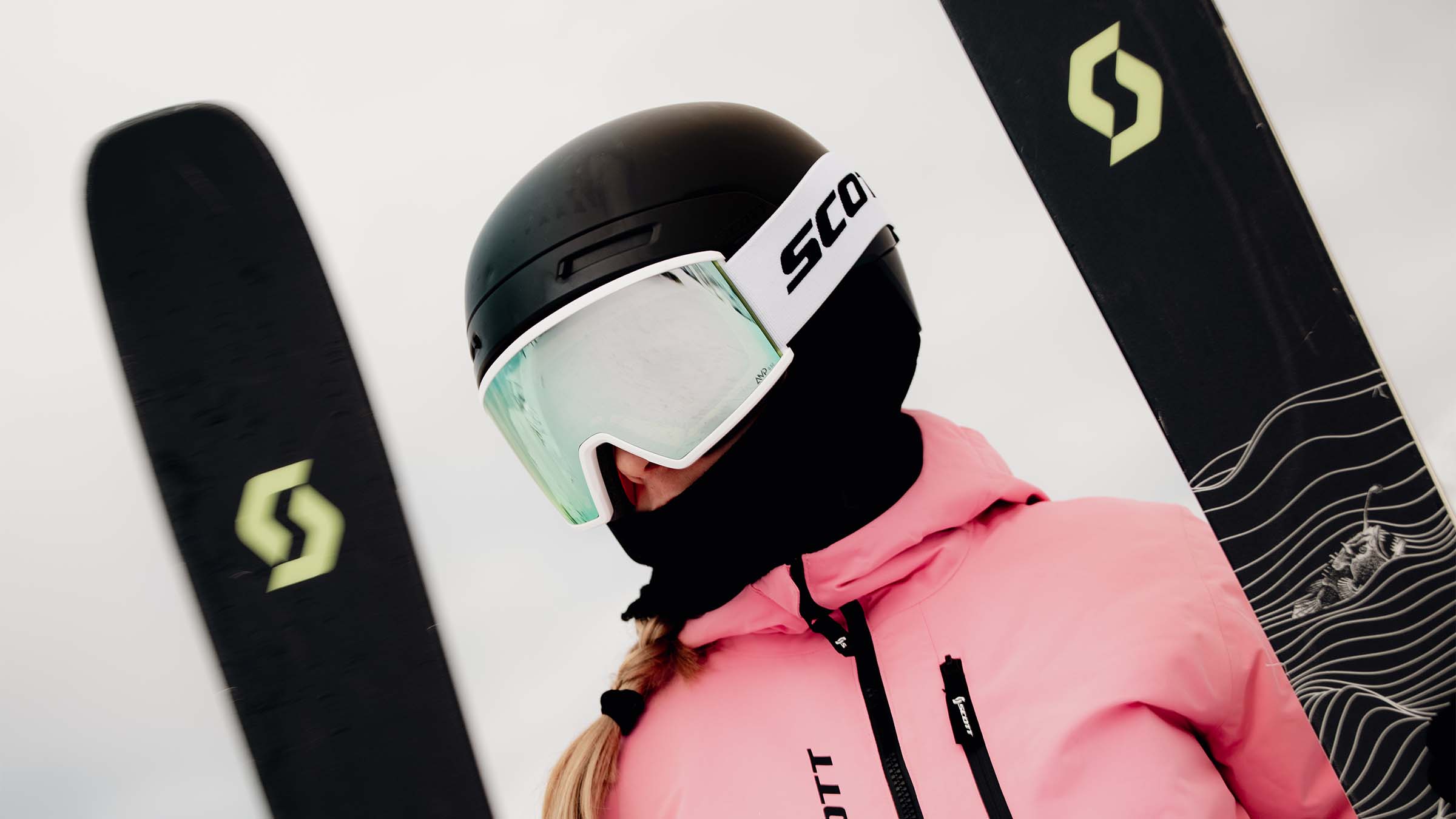 A young person wearing SCOTT goggles while holding SCOTT skis.