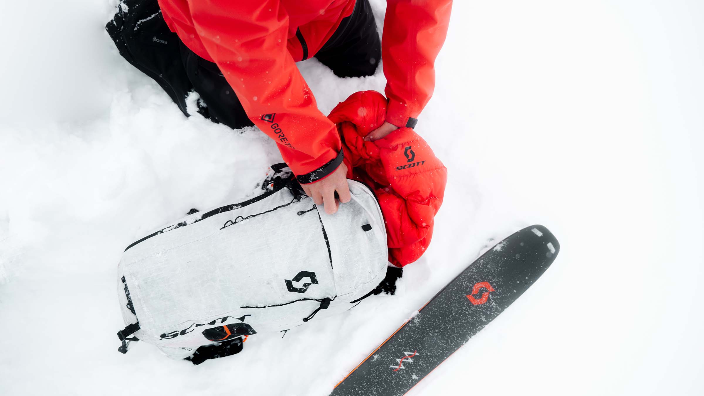 Top down view of a person putting their down jacket into a ski pack.