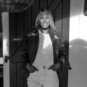 Black and white portrait of professional surfer Lakey Peterson smiling in front of a rustic barn door.