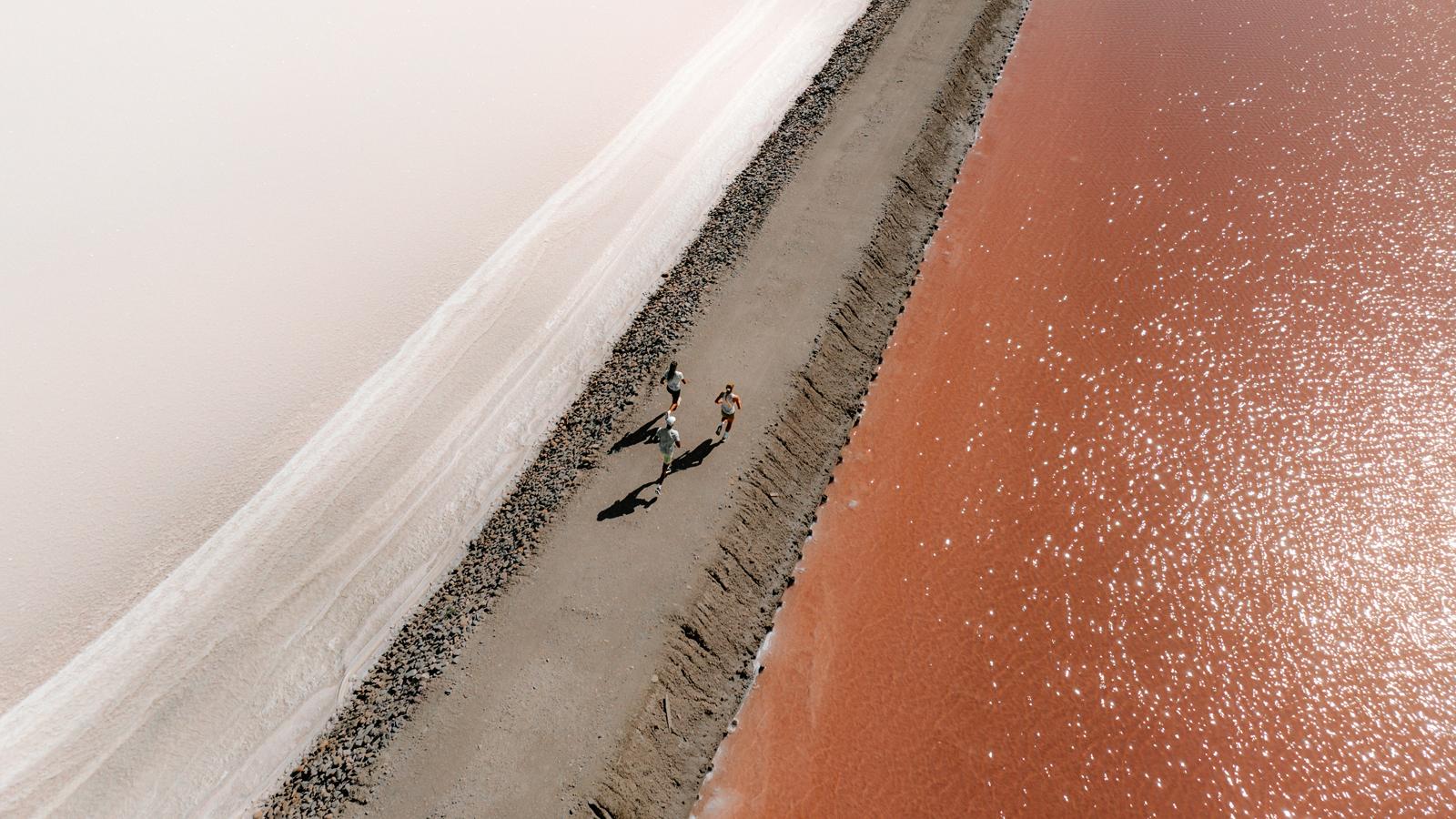 Three person running in a salt desert close to water