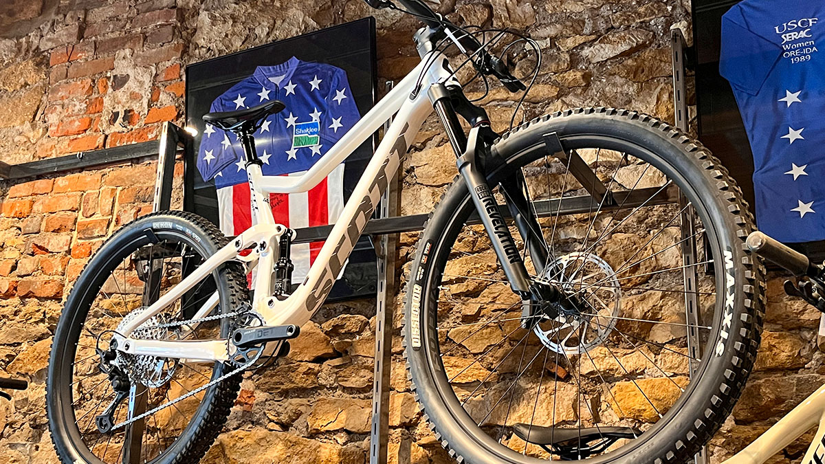 A SCOTT mountain bike hangs on a brick wall in front of a Team Skaklee National Champion jersey at Sunflower Outdoor & Bike