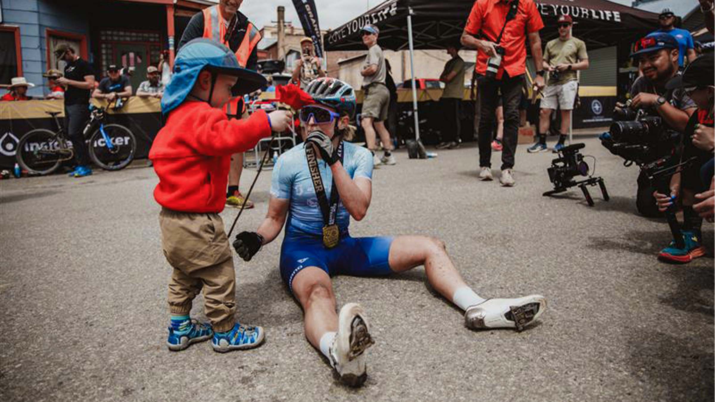 Six-time U.S. Elite National Champion, Erin Huck, sitting on the ground with her son after finishing a race.