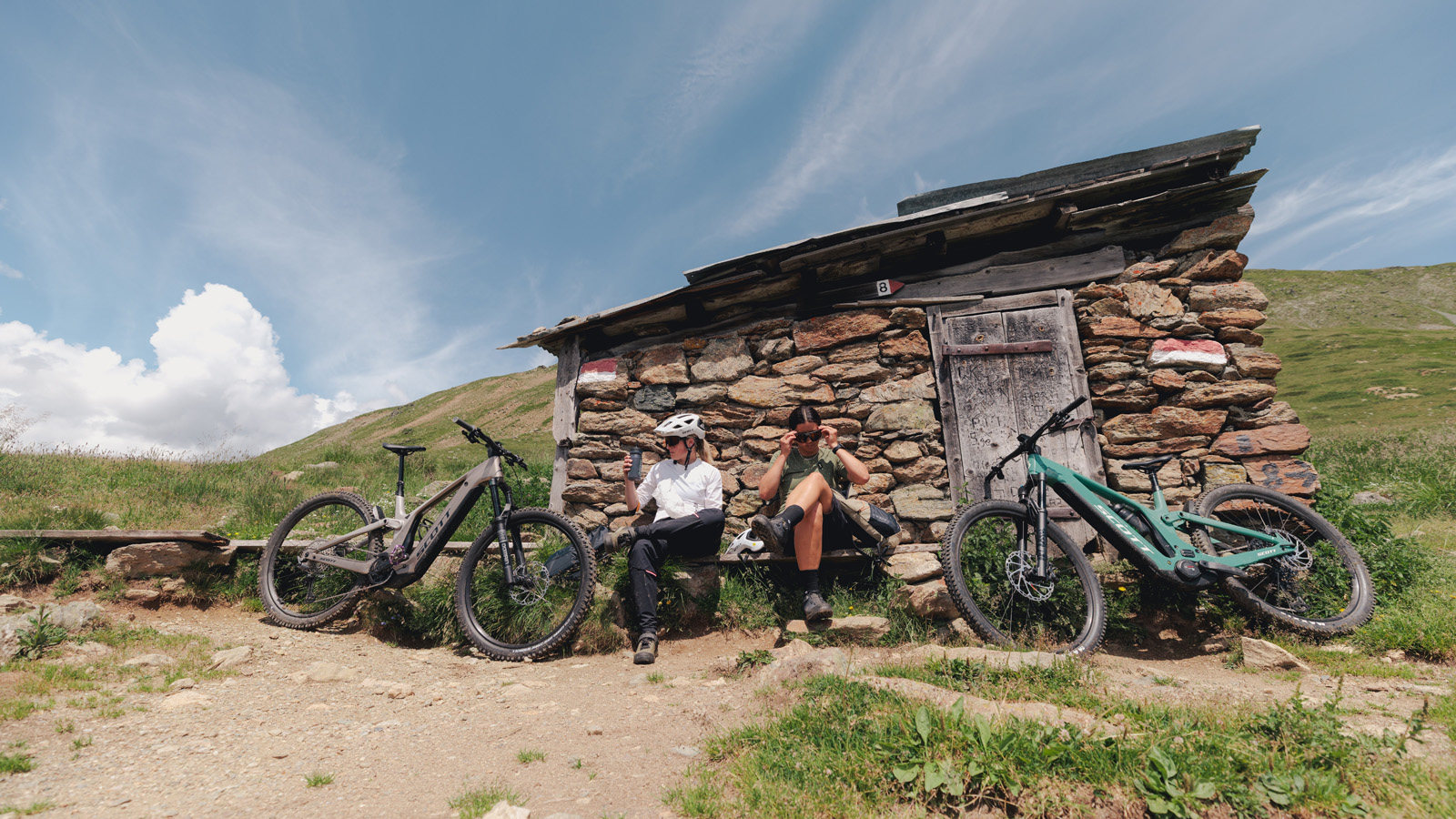 Two women taking a break and sitting on a bench in the mountains next to them SCOTT Bikes