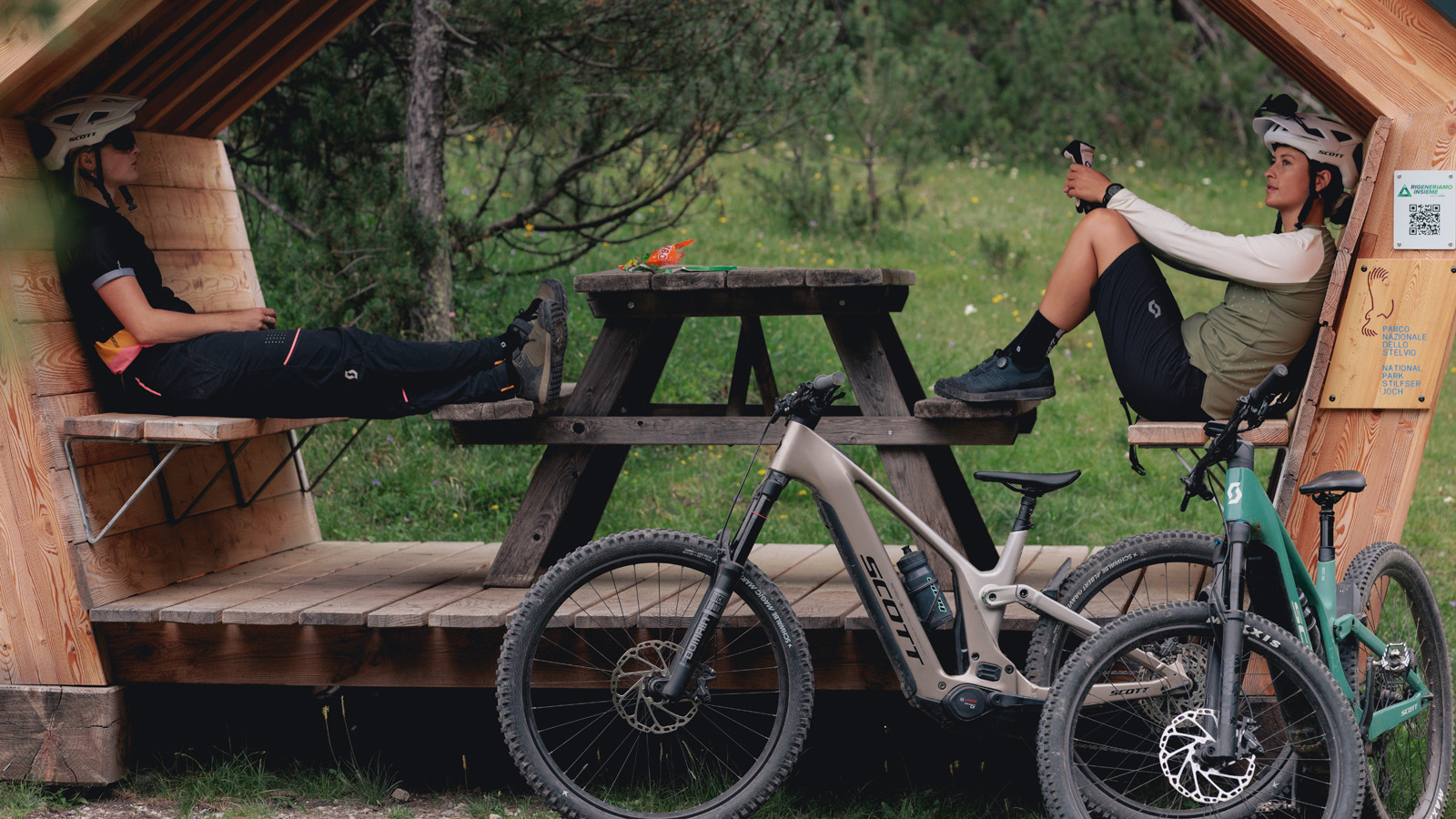 Two women taking a break and sitting on a pic nic bench with SCOTT Mountain Bike standing in front