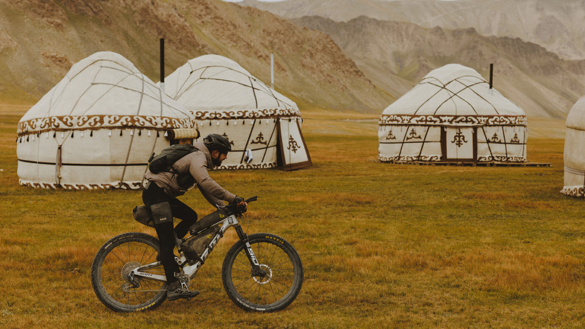 Robin Gemperle riding in front of yurts in a valley
